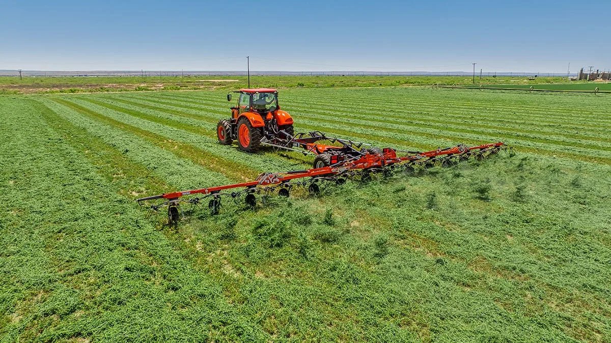 Kubota M7-134 Deluxe tractor pulling a wide Kubota tedder across a hay field