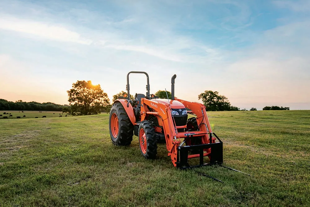 Kubota M7060 ROPS utility tractor with LA1154 loader and bale spear in a pasture at sundown