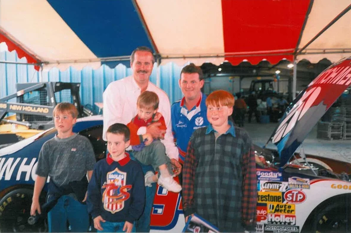 Garton family members with Ron Barfield beside a race car displaying New Holland branding