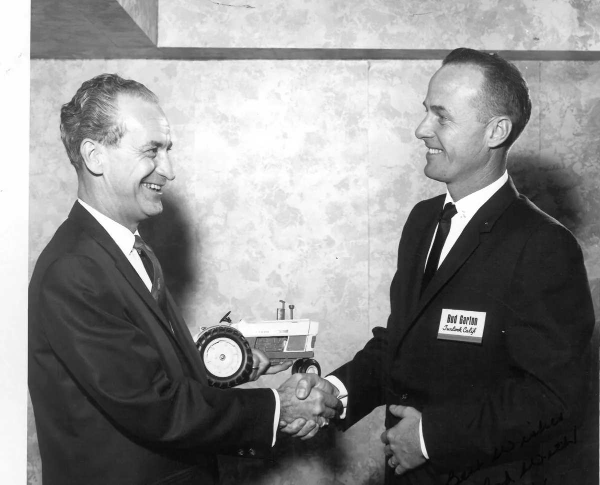 Bud Garton, wearing a name tag reading Turlock, Calif., shaking hands with a man presenting a toy Ford tractor