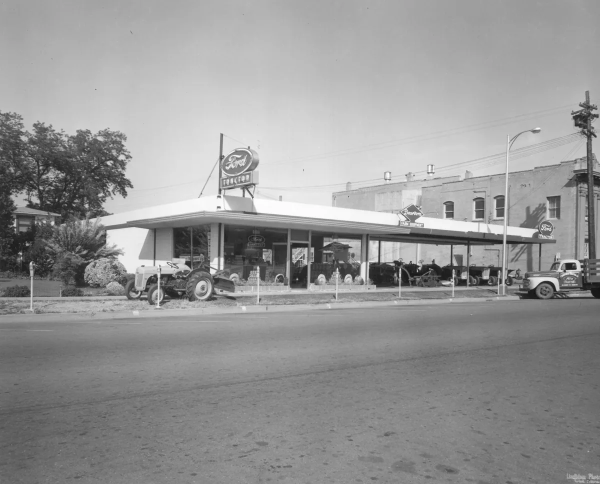 Street view of the Ford Tractor dealership with a rotating Ford Tractor sign, a Dearborn Farm Equipment sign, and tractors parked under the canopy